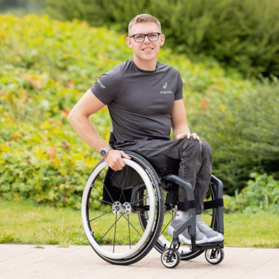 Ein junger Mann sitzt im Rollstuhl und lacht.